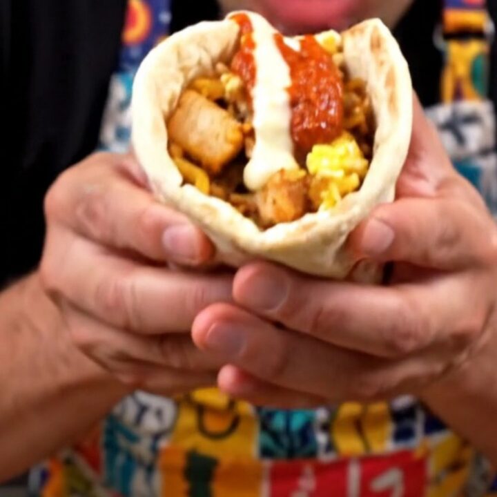 A close-up of a grilled chicken and rice breakfast wrap with scrambled eggs and garlic sauce.