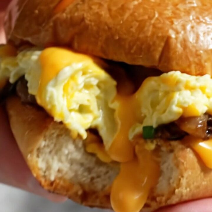 A close-up of a soft-scrambled egg sandwich on a toasted brioche bun with chives and visible melted cheddar.