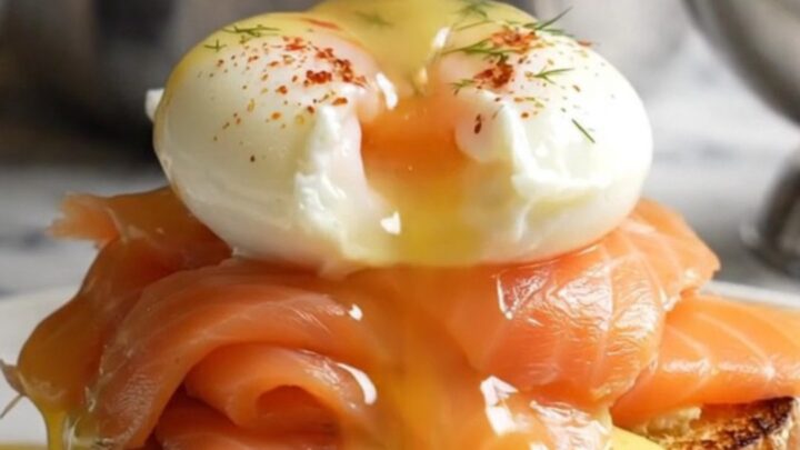A close-up of a perfectly poached egg on smoked salmon and toasted brioche, topped with velvety hollandaise.