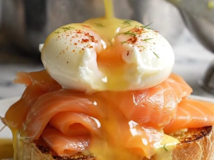 A close-up of a perfectly poached egg on smoked salmon and toasted brioche, topped with velvety hollandaise.