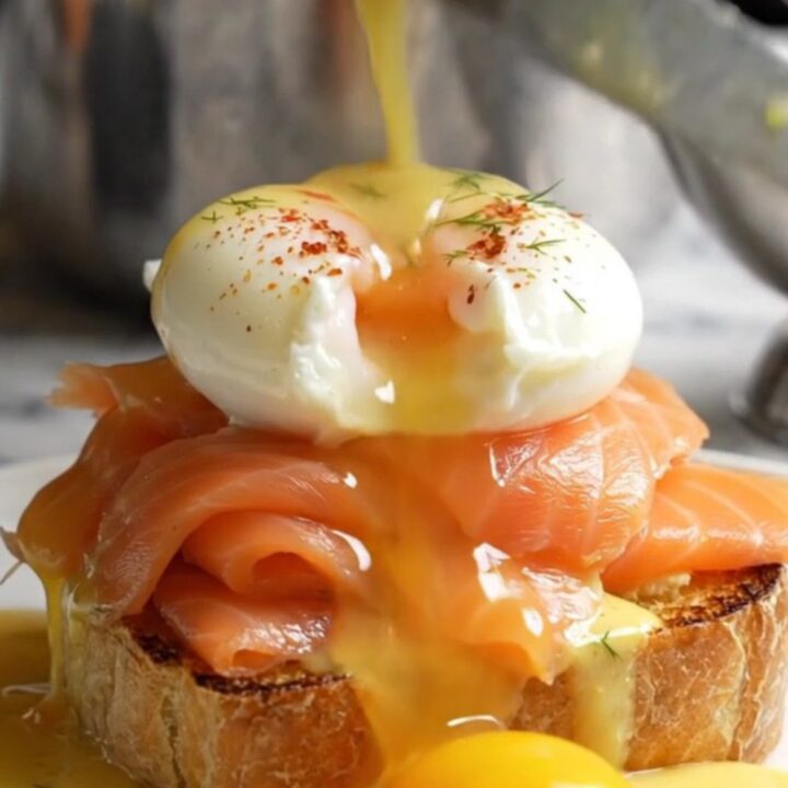 A close-up of a perfectly poached egg on smoked salmon and toasted brioche, topped with velvety hollandaise.