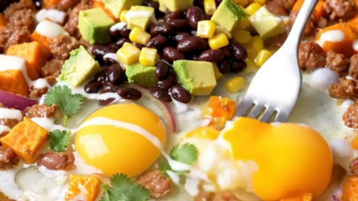 A cast-iron skillet filled with a colorful hash of sweet potatoes, chorizo, black beans, corn, and four perfectly fried eggs.