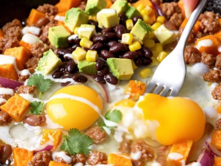 A cast-iron skillet filled with a colorful hash of sweet potatoes, chorizo, black beans, corn, and four perfectly fried eggs.
