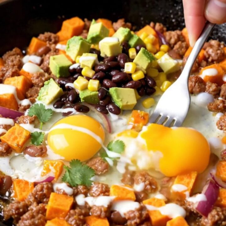 A cast-iron skillet filled with a colorful hash of sweet potatoes, chorizo, black beans, corn, and four perfectly fried eggs.