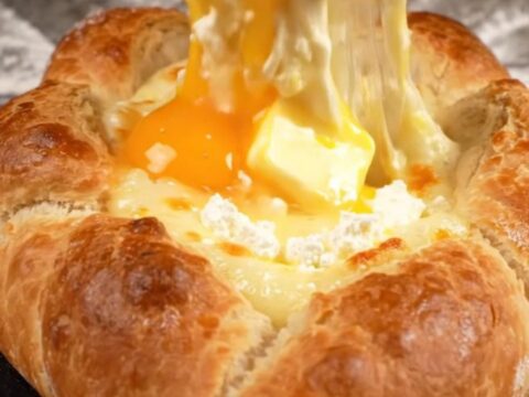 A golden-brown Georgian cheese bread boat filled with molten mozzarella and feta cheese, topped with a raw