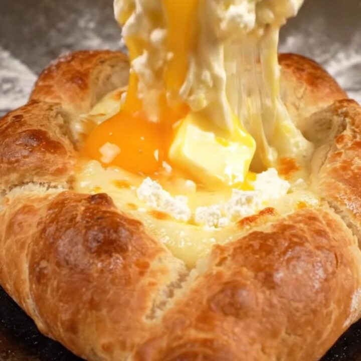 A golden-brown Georgian cheese bread boat filled with molten mozzarella and feta cheese, topped with a raw