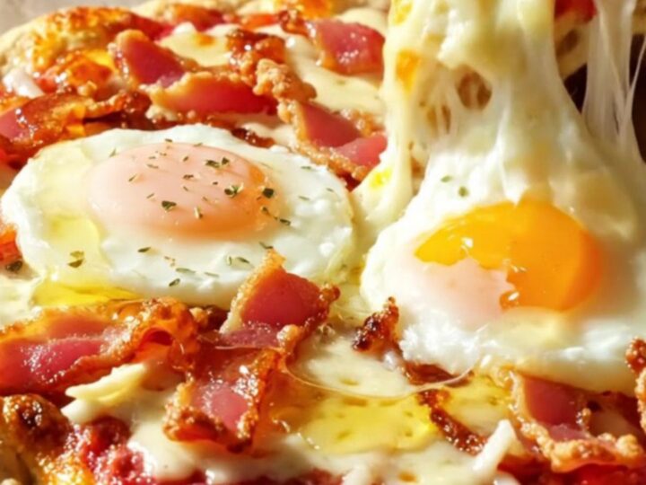 A golden cottage cheese flatbread pizza topped with melted mozzarella, crispy bacon, two baked eggs