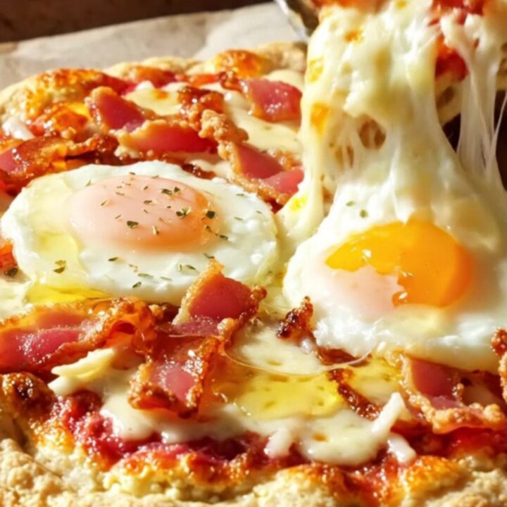 A golden cottage cheese flatbread pizza topped with melted mozzarella, crispy bacon, two baked eggs