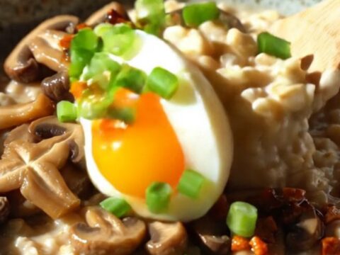 A bowl of savory oatmeal topped with sautéed shiitake mushrooms, a soft-boiled egg, and vibrant red chili crisp.