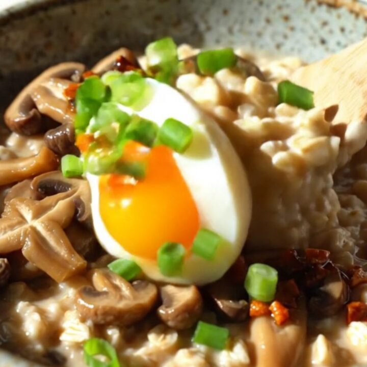 A bowl of savory oatmeal topped with sautéed shiitake mushrooms, a soft-boiled egg, and vibrant red chili crisp.