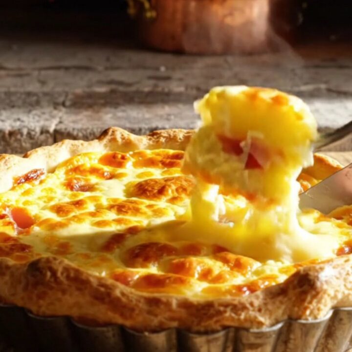 A golden-baked Quiche Lorraine with a visible, flaky crust and a rich, creamy filling, steaming on a rustic kitchen table.