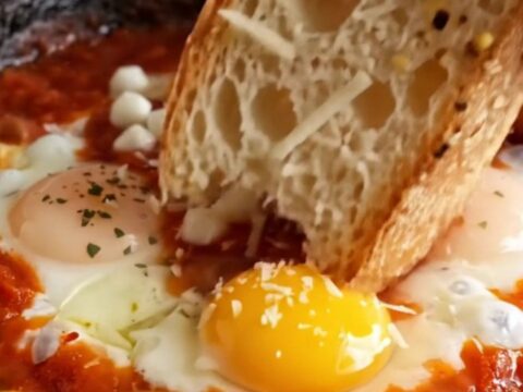 A close-up of three poached eggs in a vibrant red tomato sauce topped with melted mozzarella and herbs.