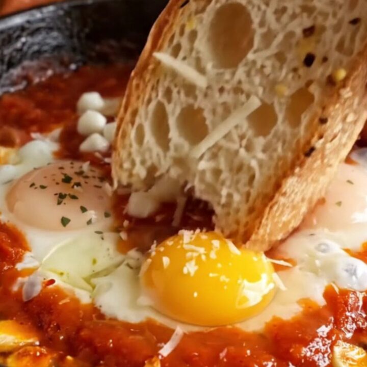 A close-up of three poached eggs in a vibrant red tomato sauce topped with melted mozzarella and herbs.