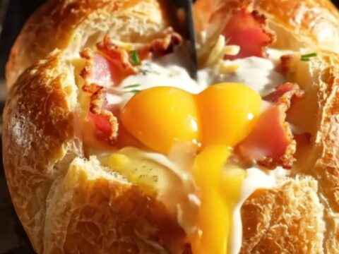 A crispy, golden-brown mini brioche boat filled with melted Gruyère, crispy bacon, and a runny egg yolk.