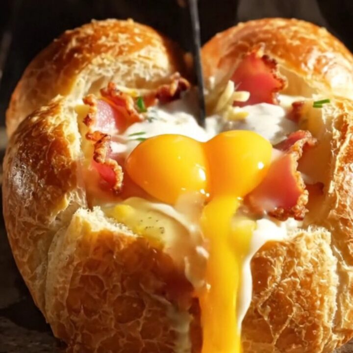 A crispy, golden-brown mini brioche boat filled with melted Gruyère, crispy bacon, and a runny egg yolk.