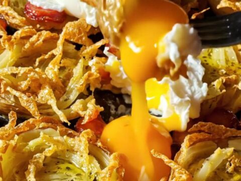A close-up of crispy smashed fingerling potatoes topped with smoky chorizo and a poached egg with a runny yolk.
