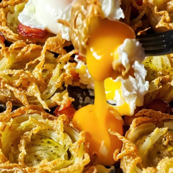 A close-up of crispy smashed fingerling potatoes topped with smoky chorizo and a poached egg with a runny yolk.