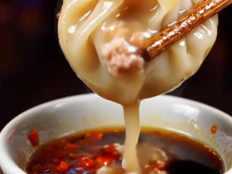 Golden crispy lace pork soup dumplings served on a dark plate with chili oil.
