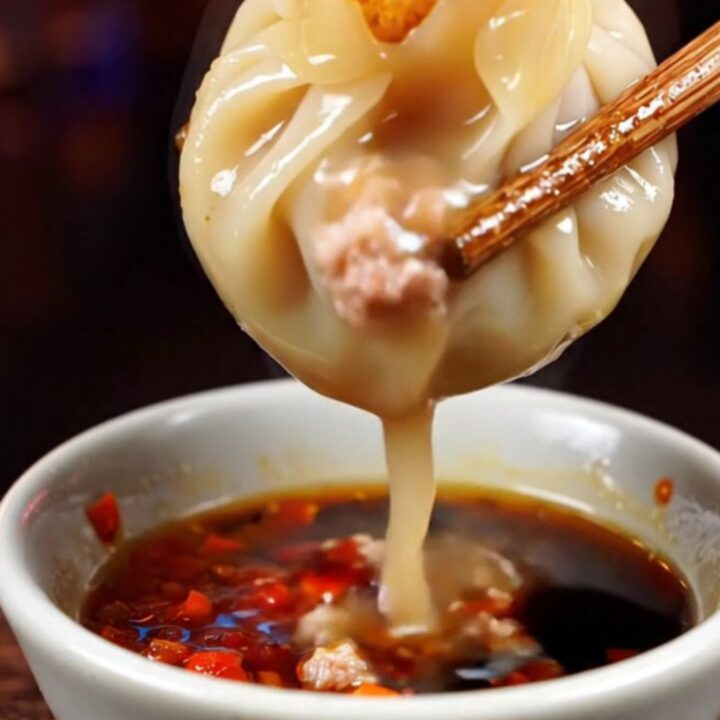Golden crispy lace pork soup dumplings served on a dark plate with chili oil.