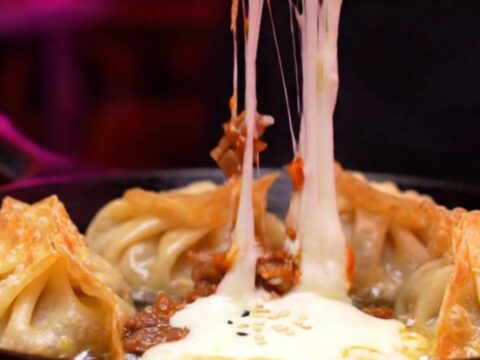 Two crispy golden mandu dumplings being pulled apart, showing a dramatic stretch of molten mozzarella cheese.