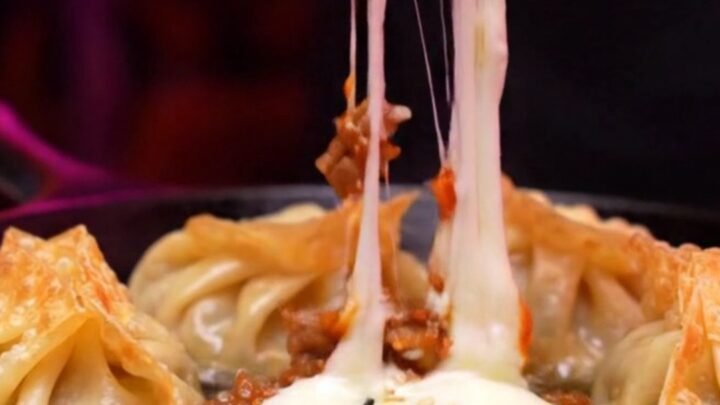 Two crispy golden mandu dumplings being pulled apart, showing a dramatic stretch of molten mozzarella cheese.