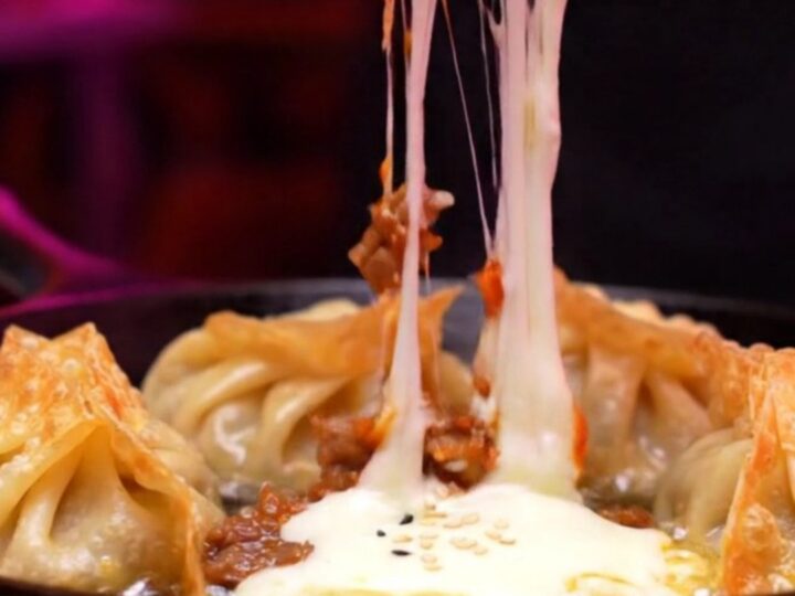 Two crispy golden mandu dumplings being pulled apart, showing a dramatic stretch of molten mozzarella cheese.