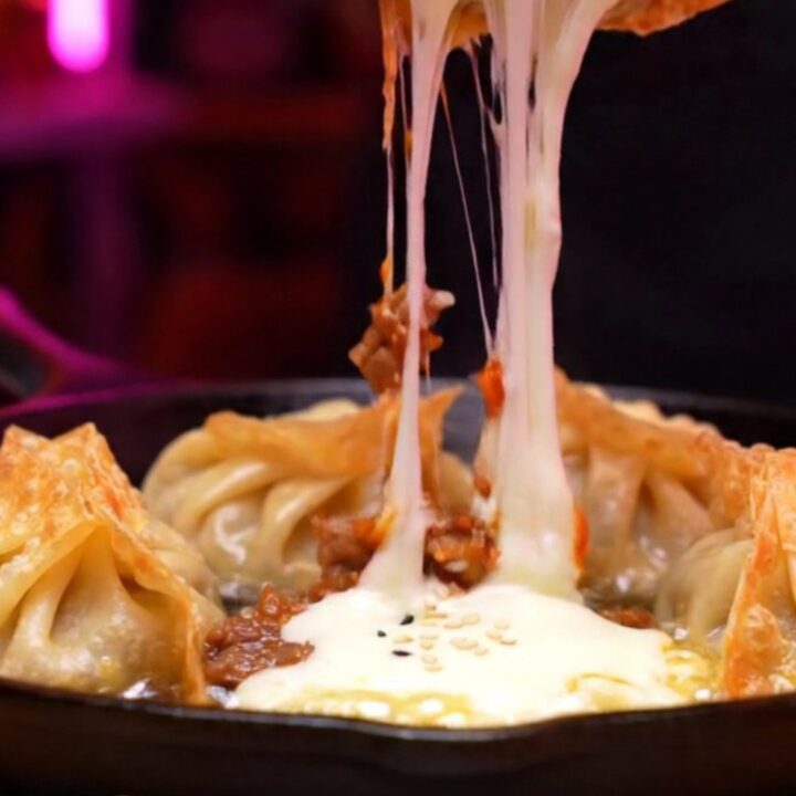 Two crispy golden mandu dumplings being pulled apart, showing a dramatic stretch of molten mozzarella cheese.