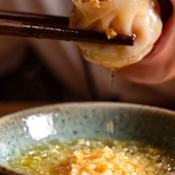 A close-up shot of crystal shrimp dumplings topped with vibrant, sizzling garlic chili crisp.