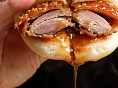 Crispy Peking duck bao slider with hoisin and cucumber on a wooden board.