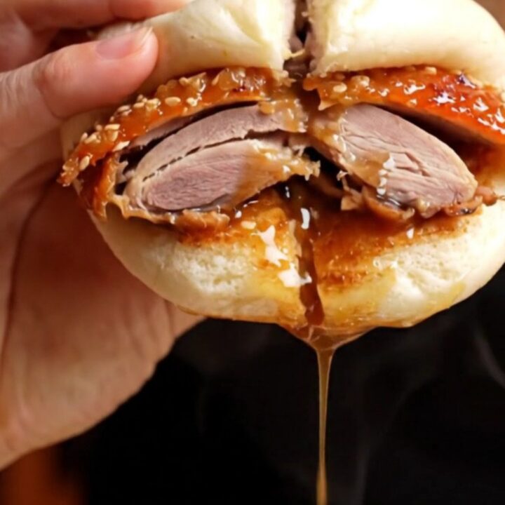 Crispy Peking duck bao slider with hoisin and cucumber on a wooden board.