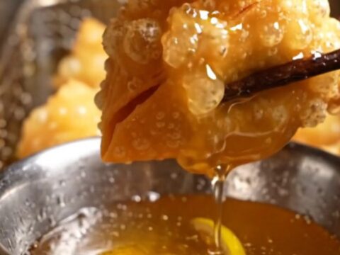 Golden, crispy lobster wonton pouches arranged on a dark plate, showing their pyramid shape and blistered texture.