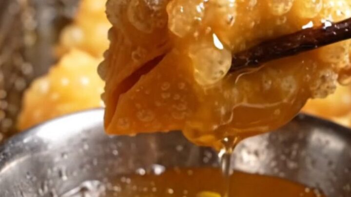 Golden, crispy lobster wonton pouches arranged on a dark plate, showing their pyramid shape and blistered texture.
