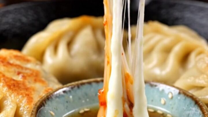 A crispy golden-brown kimchi and mozzarella dumpling being sliced in half with visible melted cheese.