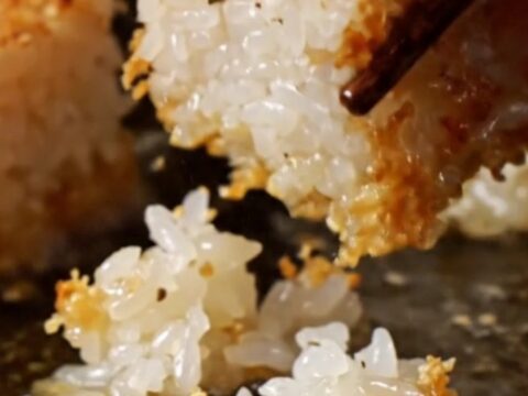 A close-up of a golden crispy rice cube topped with ruby-red spicy tuna, a jalapeño slice, and sriracha aioli.