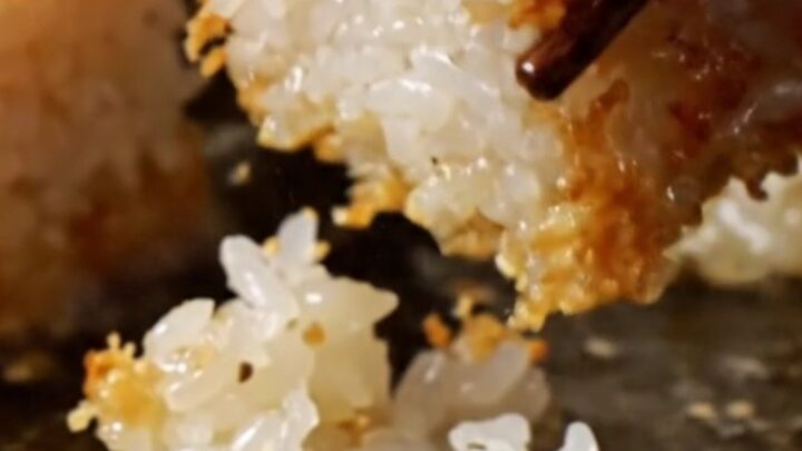 A close-up of a golden crispy rice cube topped with ruby-red spicy tuna, a jalapeño slice, and sriracha aioli.