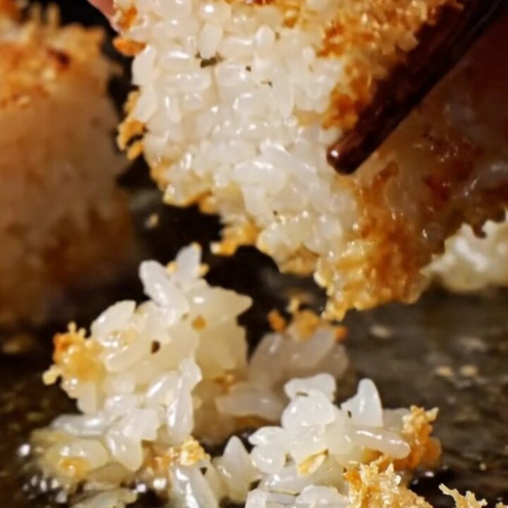 A close-up of a golden crispy rice cube topped with ruby-red spicy tuna, a jalapeño slice, and sriracha aioli.