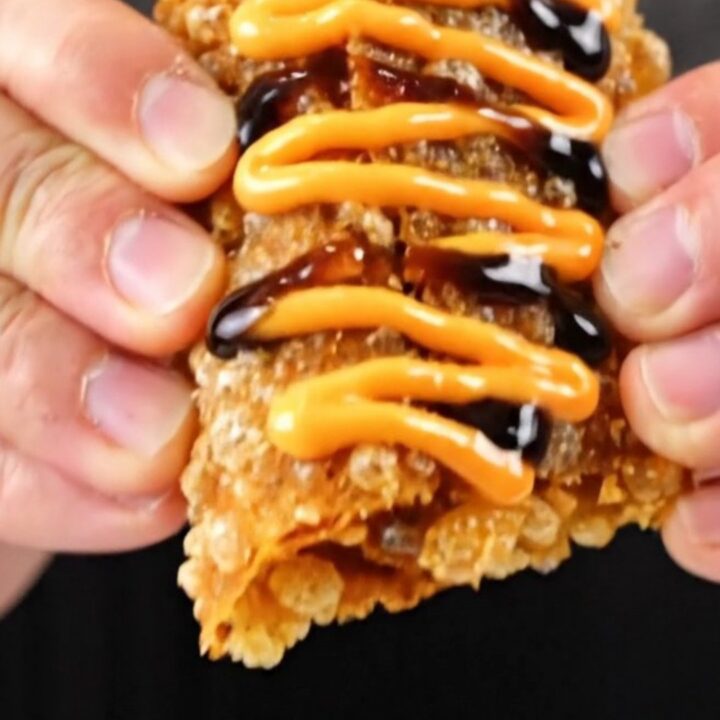 A crispy folded sushi wrap drizzled with spicy mayo and eel sauce, showing flaky salmon and avocado.