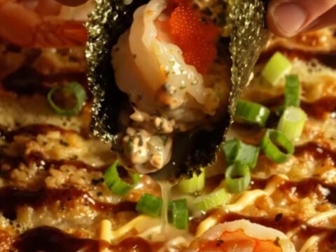 A close-up of a creamy garlic butter shrimp sushi bake in a ceramic dish, topped with scallions and masago.