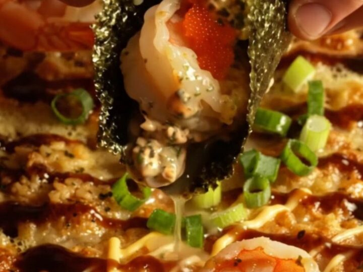 A close-up of a creamy garlic butter shrimp sushi bake in a ceramic dish, topped with scallions and masago.