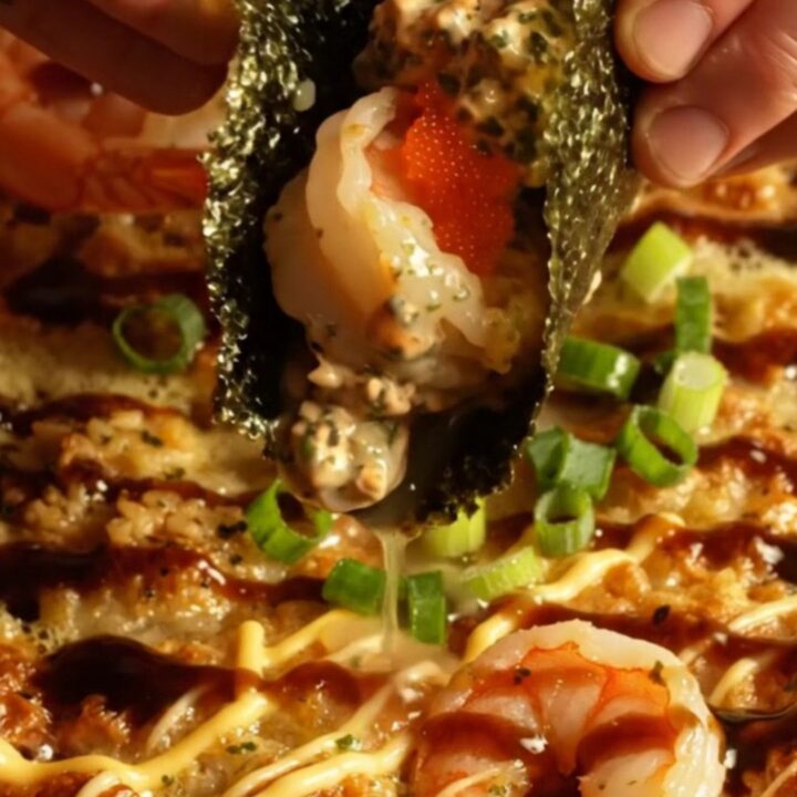 A close-up of a creamy garlic butter shrimp sushi bake in a ceramic dish, topped with scallions and masago.