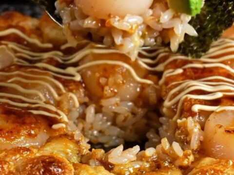 A bubbly, golden-brown scallop sushi bake in a square dish topped with bright orange tobiko.