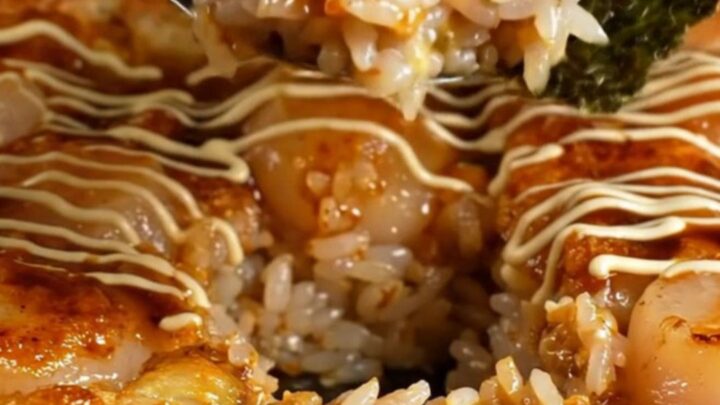 A bubbly, golden-brown scallop sushi bake in a square dish topped with bright orange tobiko.