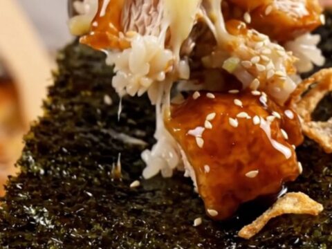 A close-up of a bubbling sushi bake in a casserole dish topped with crispy onions and scallions.