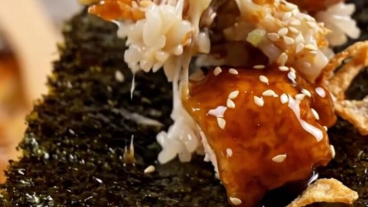 A close-up of a bubbling sushi bake in a casserole dish topped with crispy onions and scallions.