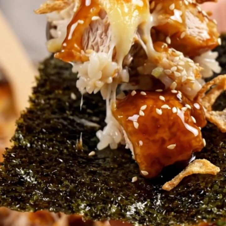 A close-up of a bubbling sushi bake in a casserole dish topped with crispy onions and scallions.