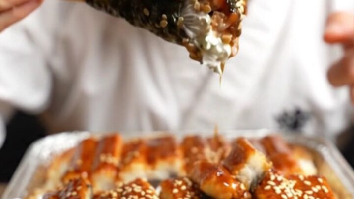 A close-up of a creamy unagi sushi bake in a baking dish, featuring a caramelized glaze and avocado layers.