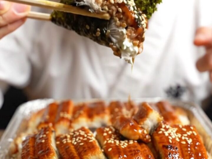 A close-up of a creamy unagi sushi bake in a baking dish, featuring a caramelized glaze and avocado layers.