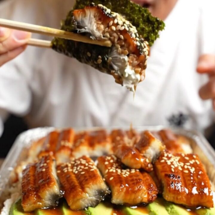 A close-up of a creamy unagi sushi bake in a baking dish, featuring a caramelized glaze and avocado layers.