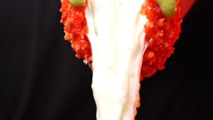 A close-up shot of a Flamin Hot Cheetos crusted Korean corn dog with a long, stretchy mozzarella cheese pull.