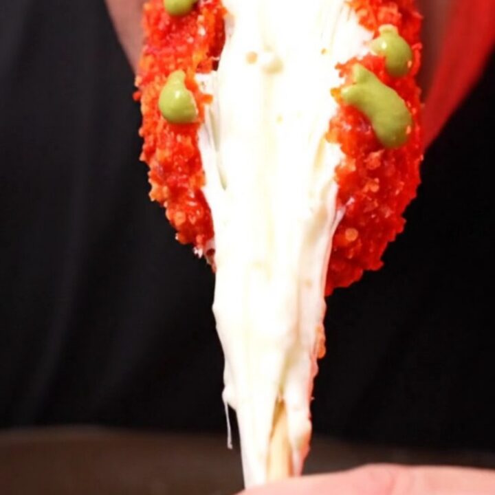 A close-up shot of a Flamin Hot Cheetos crusted Korean corn dog with a long, stretchy mozzarella cheese pull.